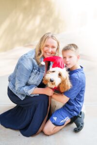 Mother and son hug dog dressed up in Santa Clause hat.